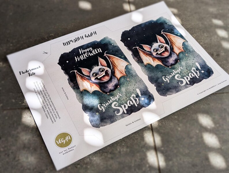 May include: Two printable Halloween treat bags featuring a cute cartoon bat with a toothy grin. The bags are decorated with a starry night sky background and the text "Happy Halloween" and "Gruseliger Spa&szlig;!" which translates to "Spooky Fun!" in English.