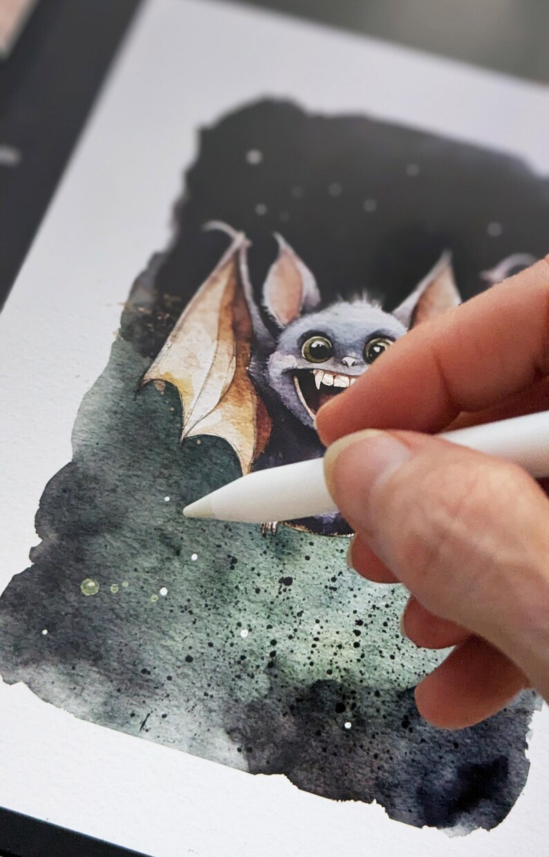 May include: A digital illustration of a cartoon bat with large eyes and a toothy grin. The bat is drawn in a watercolor style with a dark green and black background. The artist is using a stylus to add details to the illustration.