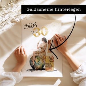 May include: A watercolor illustration of a woman holding a glass of champagne, sitting on a globe. The text "CHEERS TO 30" is written above her. The image is on a white background with a hand holding a 50 euro bill over the illustration. The text "Geldscheine hinterlegen" is written above the hand.