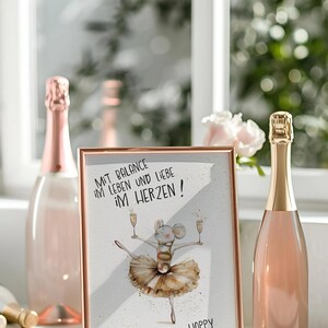 May include: A white framed picture with a gold border. The picture features a cartoon mouse wearing a tutu and holding two glasses of champagne. The text on the picture reads "Mit Balance im Leben und Liebe im Herzen! Happy Birthday!"