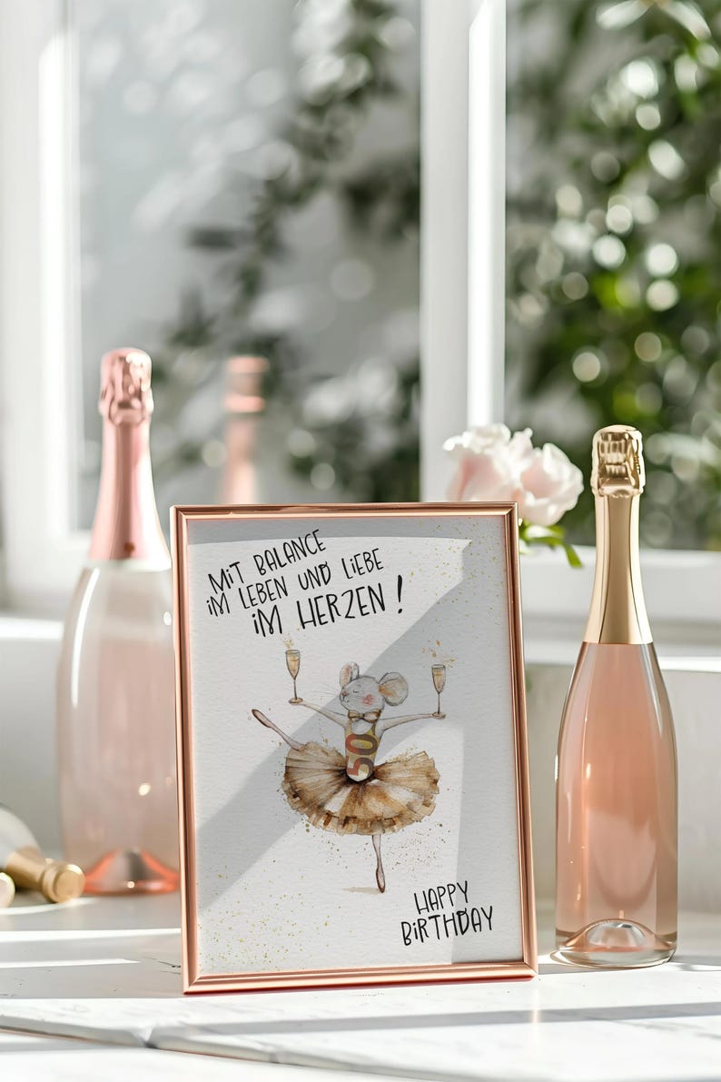 May include: A white framed picture with a gold border. The picture features a cartoon mouse wearing a tutu and holding two glasses of champagne. The text on the picture reads "Mit Balance im Leben und Liebe im Herzen! Happy Birthday!"