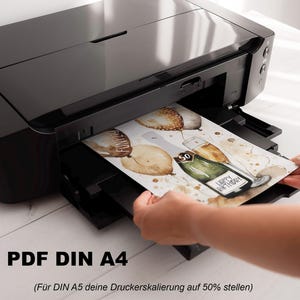 May include: A black printer with a white sheet of paper being inserted into the paper tray. The paper has a watercolor illustration of balloons, a bottle of champagne, and the text "Happy Birthday". The text "PDF DIN A4 (For DIN A5, set your printer scaling to 50%)" is printed below the image.
