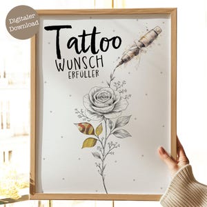 Op de afbeelding: Een ingelijste print met een tattoo-ontwerp. Het kunstwerk bevat het woord "Tattoo", een tattoo-machine en een gedetailleerde rozenillustratie. De print heeft een lichte houten lijst met een gestippelde achtergrond. De tekst "Wunsch Erfüller" is ook zichtbaar.
