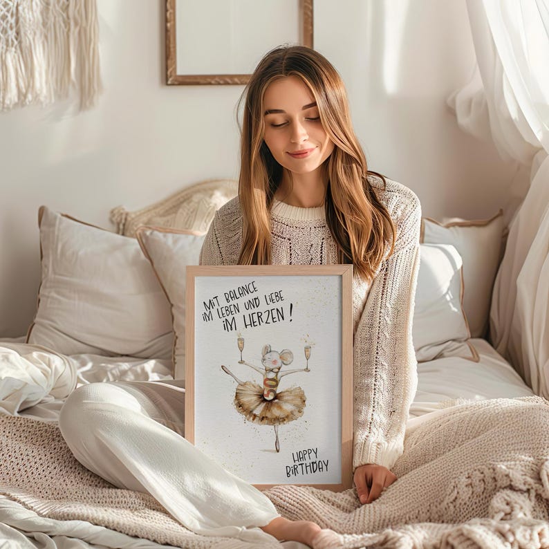 May include: A framed print with a watercolor illustration of a mouse wearing a tutu and holding champagne glasses. The text on the print reads "Mit Balance im Leben und Liebe im Herzen! Happy Birthday!"