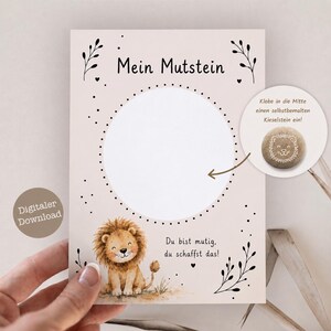 May include: A digital download card with a light pink background. The card features a lion illustration, the text "Mein Mutstein", and a space for a painted stone. Additional text includes "Du bist mutig, du schaffst das!" and "Klebe in die Mitte einen selbstbemalten Kieselstein ein!"