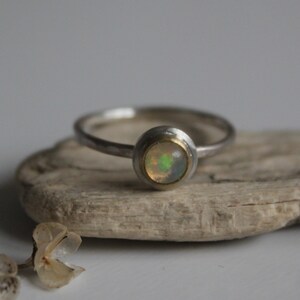 Könnte beinhalten: Ein silberner Ring mit einem goldenen Band und einem runden Opal-Edelstein.