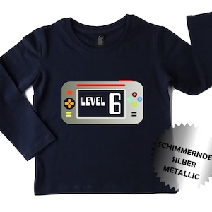 May include: Navy blue long-sleeve shirt with a graphic of a video game console. The console has a screen that says "LEVEL 6".