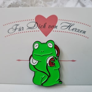Könnte beinhalten: Grüner Frosch mit roten Kopfhörern mit weißen Ohrmuscheln. Der Frosch sitzt auf einer weißen Karte mit dem Text "Für Dich von Herzen" in Schwarz.