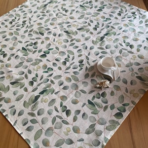 Peut inclure: Une nappe blanche avec un motif de feuilles d'eucalyptus vertes. La nappe est en lin et a une texture subtile.