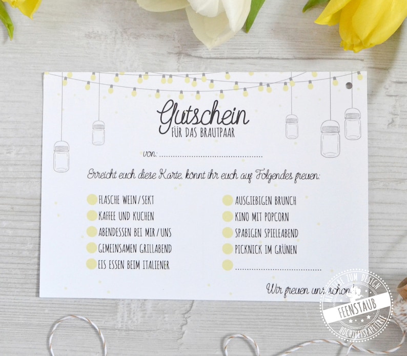 May include: A white card with the text "Gutschein F&Uuml;R DAS BRAUTPAAR" in elegant script. The card features illustrations of hanging mason jars and string lights. The card lists various experiences, such as wine, brunch, and a picnic.