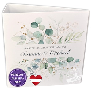 Könnte beinhalten: Weißer Hochzeitsplaner-Ordner mit einem Aquarell-Eukalyptus- und Goldblatt-Design. Der Text "Unsere Hochzeitsplanung Susanne & Michael" ist auf der Vorderseite gedruckt. Ein lila Kreis mit dem Text "PERSON-ALISIER-BAR" und ein rotes Herz mit der österreichischen Flagge sind ebenfalls sichtbar.