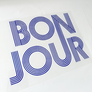 Könnte beinhalten: Ein transparenter Vinyl-Aufkleber mit dem Wort "BONJOUR" in blauen umrandeten Buchstaben. Die Buchstaben bestehen aus mehreren parallelen Linien.