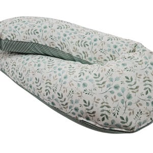 May include: A large, U-shaped pillow with a botanical leaf pattern in shades of green and grey on a white background. The pillow has a green textured border and is designed for comfort and support.