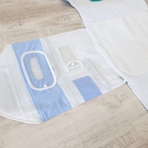 May include: A white and light blue baby changing mat with multiple pockets and compartments. The mat is folded open to reveal a clear plastic pocket, a blue polka dot pocket, and a white pocket with a white zipper. The mat is made of a soft, quilted fabric and is perfect for keeping all of your baby's essentials organized.