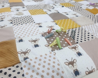 May include: A multi-colored baby quilt with a patchwork design. The quilt features various fabrics, including polka dots, stripes, and animal prints. There are several brown, green, and yellow ribbons attached to the quilt.
