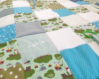Peut inclure: Une courtepointe en patchwork composée de carrés de tissu dans des tons de bleu, vert et blanc. Le motif présente des personnages vikings, des navires, des étoiles et des pois, avec un carré central brodé du prénom Eyvin.