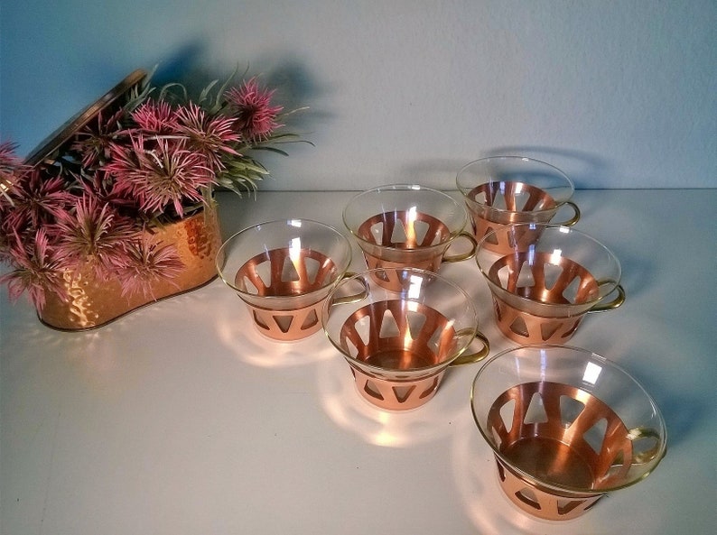 May include: Set of six clear glass teacups with copper colored metal bases. The cups have a geometric design and gold colored handles.