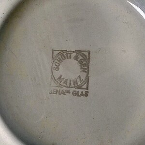 May include: A white ceramic plate with a black and white logo that reads "Schott & Gen Jenaer Glas" in a circle.