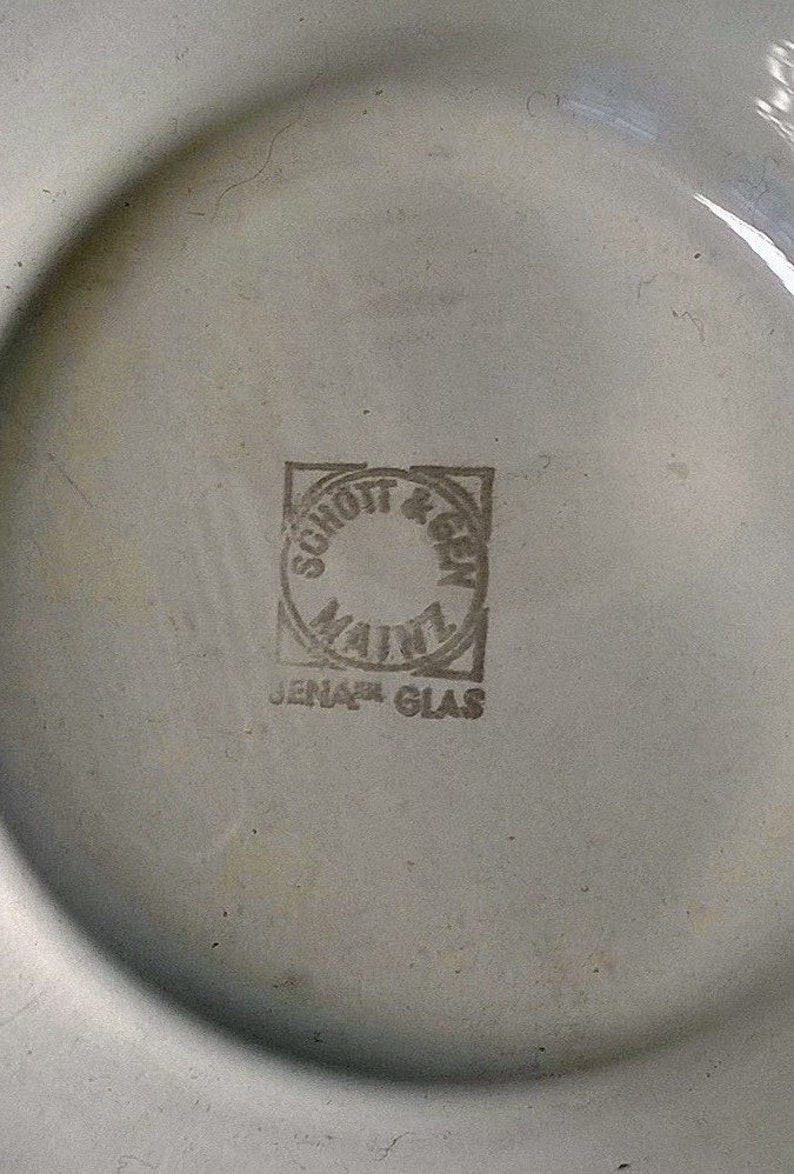 May include: A white ceramic plate with a black and white logo that reads "Schott & Gen Jenaer Glas" in a circle.