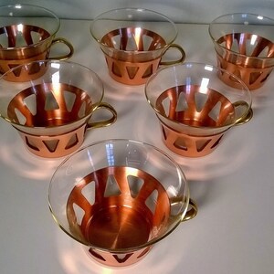 May include: Set of six copper and glass teacups with a geometric design. The cups have a clear glass bowl with a copper band around the top and a copper handle.
