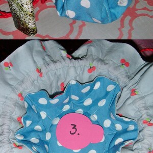 May include: A blue and white polka dot fabric pouch with a drawstring closure. The pouch is lined with a light blue fabric with a cherry print. A pink label with the number "3." is attached to the pouch.