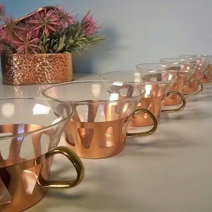 May include: Set of six copper and glass cups with brass handles. The cups have a unique design with cutouts in the copper band.