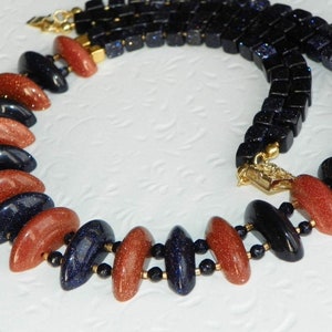 May include: A necklace made with alternating blue and brown gemstone beads. The beads are faceted and have a sparkly finish. The necklace is strung on a gold chain.