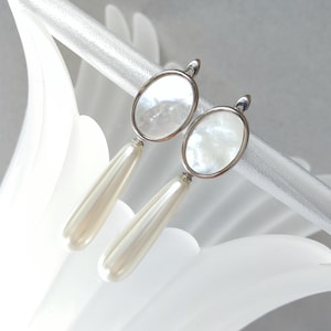 May include: A pair of silver clip-on earrings with white oval-shaped mother-of-pearl stones and white pearl drops.