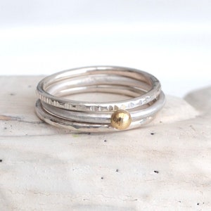 Könnte beinhalten: Drei silberne Stapelringe mit einem kleinen goldenen Perlenakzent. Die Ringe sind texturiert und haben eine gehämmerte Oberfläche.