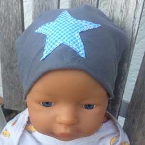 Op de afbeelding: Een grijze baby muts met een blauwe en witte geruite ster aan de voorkant.