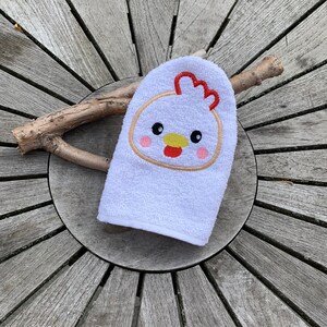Pode incluir: Toalha de banho branca com um rosto de frango bordado. O frango tem uma crista vermelha, um bico amarelo e bochechas rosadas.