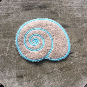May include: A beige fabric seashell with a blue embroidered spiral design.