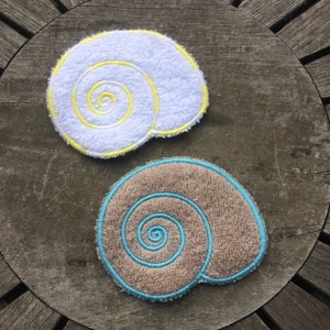 May include: Two embroidered fabric seashells, one white with yellow stitching and one brown with blue stitching.