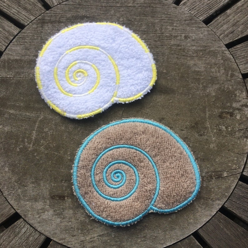 May include: Two embroidered fabric seashells, one white with yellow stitching and one brown with blue stitching.