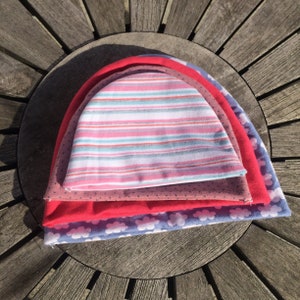 May include: Four colourful knitted hats stacked on top of each other. The top hat is pink and white striped, the second hat is brown with white polka dots, the third hat is red, and the bottom hat is blue with white clouds.