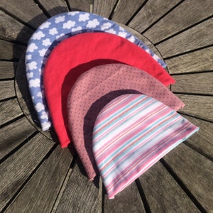 May include: Four different fabric hats stacked on top of each other. The top hat is blue with white clouds, the second hat is red, the third hat is pink with white polka dots, and the bottom hat is pink and white striped.