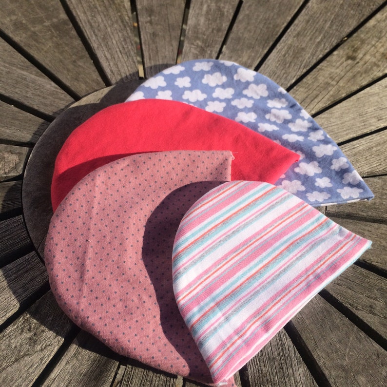 May include: Four fabric hats in different patterns and colours. The hats are stacked on top of each other. The top hat is blue with white clouds, the second hat is red, the third hat is pink with white polka dots, and the bottom hat is white with pink and blue stripes.