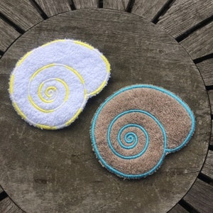 May include: Two embroidered fabric seashells, one white with yellow stitching and one brown with blue stitching.
