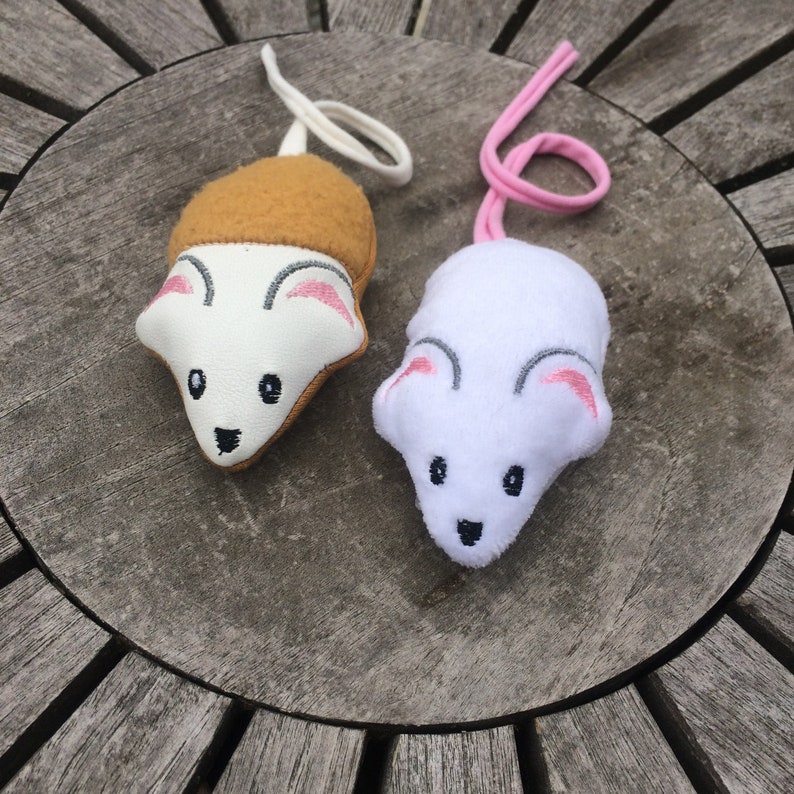 May include: Two plush toy mice with embroidered faces. One mouse is white with pink ears and a white tail. The other mouse is white with brown fur on its back and a cream-colored tail.