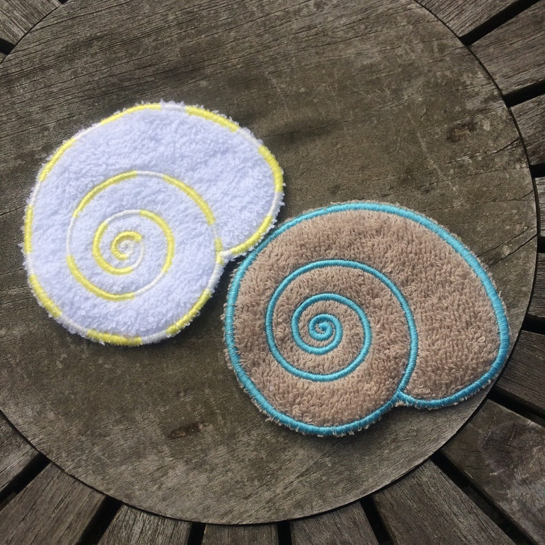 May include: Two embroidered fabric seashells, one white with yellow stitching and one brown with blue stitching.