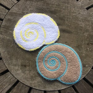 May include: Two embroidered seashell shapes, one white with yellow stitching and one brown with blue stitching.