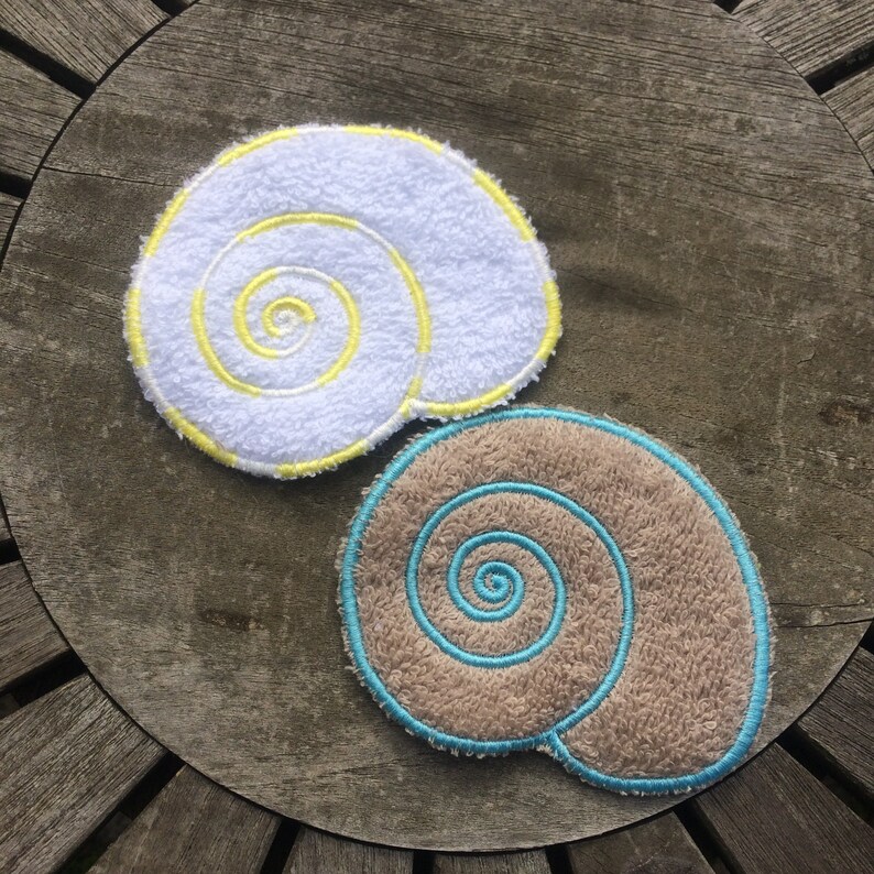 May include: Two embroidered seashell shapes, one white with yellow stitching and one brown with blue stitching.