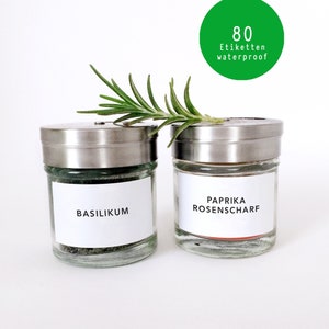 Könnte beinhalten: Zwei Gewürzgläser mit silbernen Deckeln, beschriftet mit "BASILIKUM" und "PAPRIKA ROSENSCHARF". Ein Rosmarinzweig liegt obenauf. Ein grüner Kreis mit dem Text "80 Etiketten waterproof" befindet sich im Hintergrund.