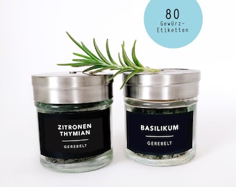 May include: Two glass spice jars with silver lids and black labels. One jar is labeled "Zitronen Thymian" and the other "Basilikum". A sprig of rosemary rests on top. A light blue circle with the text "80 Gewürz-Etiketten" is in the background.