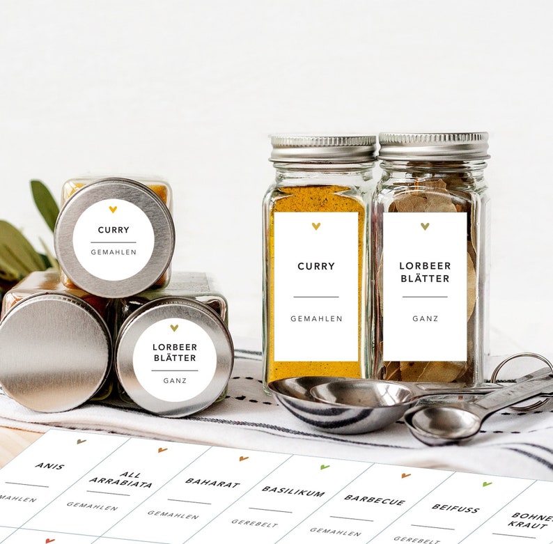 May include: A collection of spice jars with metal lids and labels. The labels read "CURRY" and "LORBEER BL&Auml;TTER". The jars are filled with yellow and brown spices. A sheet of spice labels is visible.