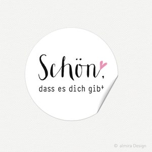 Könnte beinhalten: Weißer runder Aufkleber mit schwarzem Text "Schön, dass es dich gibt" und einem rosa Herz.