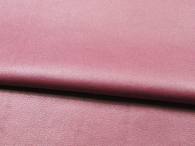 May include: A close-up of a folded piece of pink faux leather fabric with a textured surface.