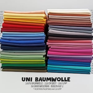 Könnte beinhalten: Zwei Stapel gefalteter Stoffe in einer Vielzahl von Unifarben, darunter Rot-, Blau-, Grün-, Gelb-, Rosa-, Lila-, Braun- und Neutraltöne. Jede Farbe ist mit einem Zahlencode versehen. Der Text am unteren Rand lautet UNI BAUMWOLLE.