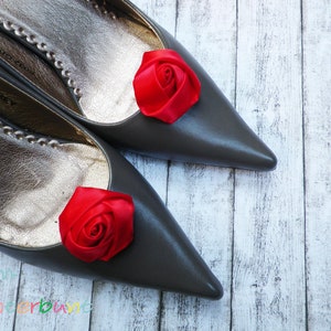 Pu&ograve; includere: Un paio di scarpe grigie a punta con decorazioni di rose in raso rosso sulle dita.