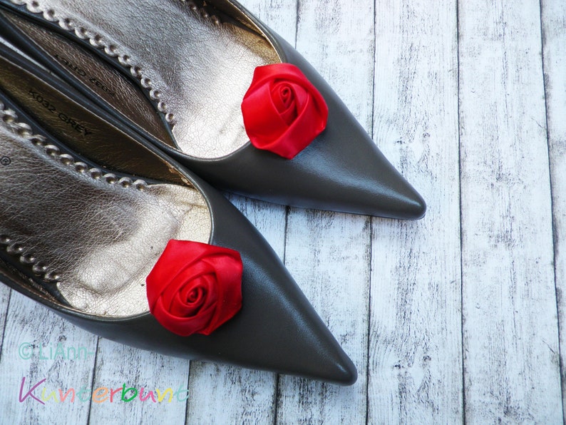 Pu&ograve; includere: Un paio di scarpe grigie a punta con decorazioni di rose in raso rosso sulle dita.